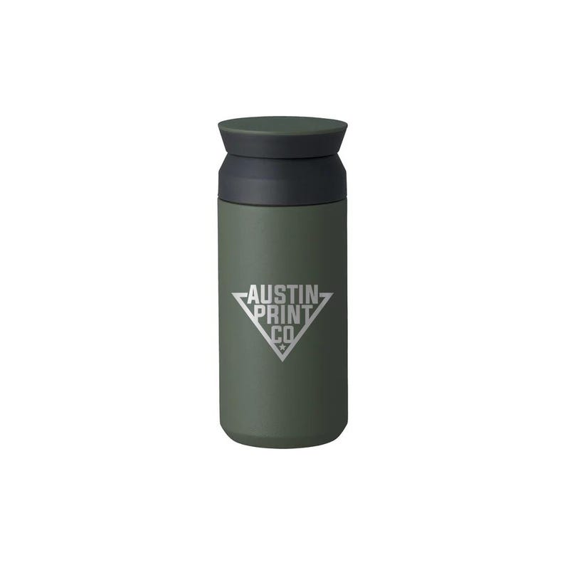 Pu&ograve; includere: Un bicchiere da viaggio verde oliva con coperchio e bordo neri. Il bicchiere presenta il testo bianco "AUSTIN PRINT CO" all'interno di un rombo bianco. Il bicchiere &egrave; cilindrico e sembra essere in metallo.