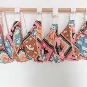 Peut inclure: Six sacs bandoulière colorés avec un motif géométrique rose, bleu, marron et vert sont suspendus à une tringle en bois. Chaque sac a une fermeture éclair dorée et une sangle blanche. Accessoire de mode.