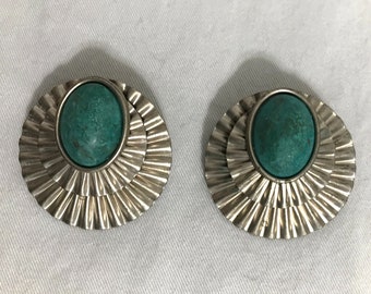 May include: A pair of silver earrings with a teal green oval stone set in the center of each earring. The earrings have a layered, fan-shaped design.