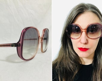 May include: A pair of pink and brown oversized sunglasses with a gradient lens. The sunglasses have a rounded square shape and a thin frame.