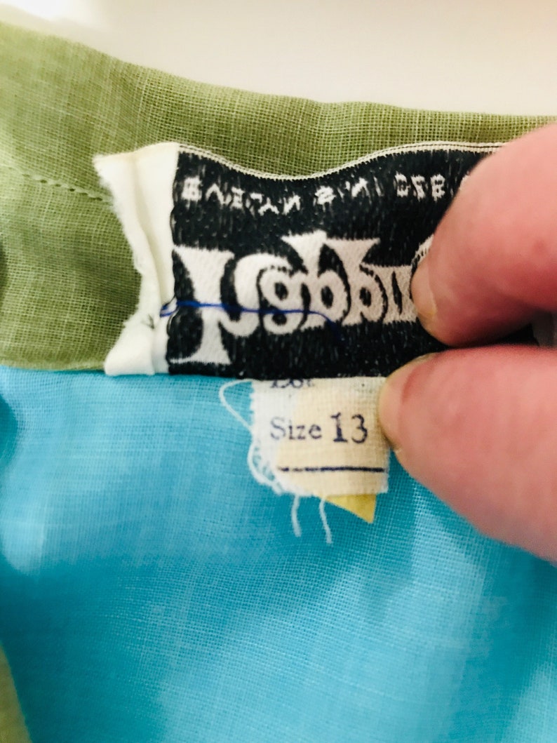 May include: A blue and green children's dress with a black label that says "Wigwam" and "Size 13".