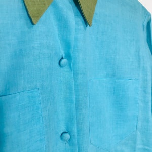 May include: A light blue linen shirt with a green collar and two buttons. The shirt has a pocket on the left side.