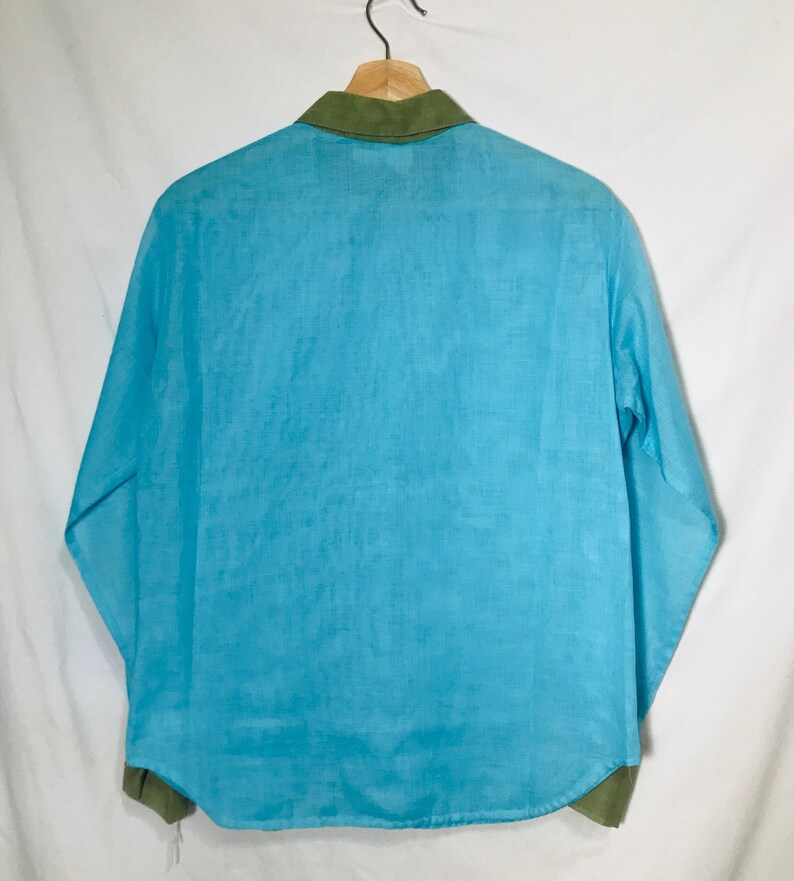 May include: A light blue long-sleeved shirt with a green collar. The shirt is made of a lightweight fabric.