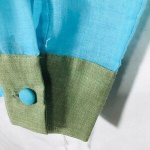 May include: Close-up of a blue and green fabric cuff with a blue button. The fabric is textured and has a subtle sheen.