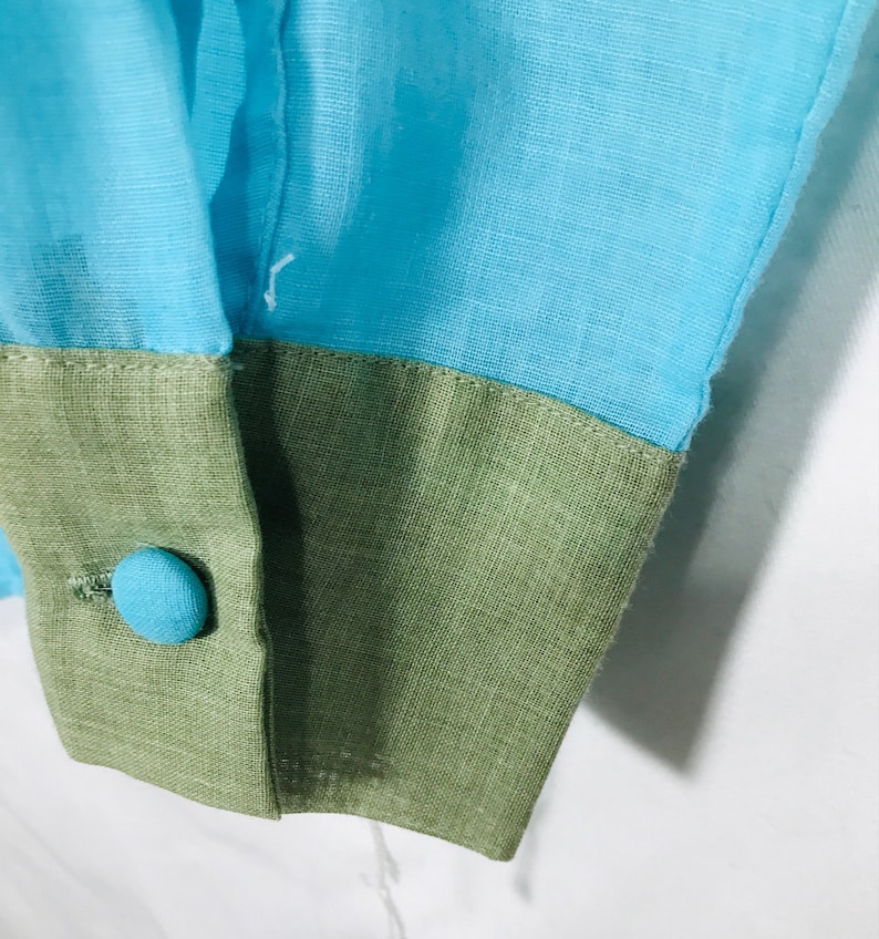 May include: Close-up of a blue and green fabric cuff with a blue button. The fabric is textured and has a subtle sheen.