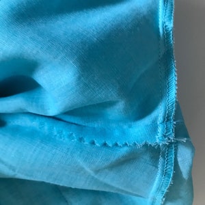May include: Close-up of a turquoise blue fabric with a stitched seam along the edge.