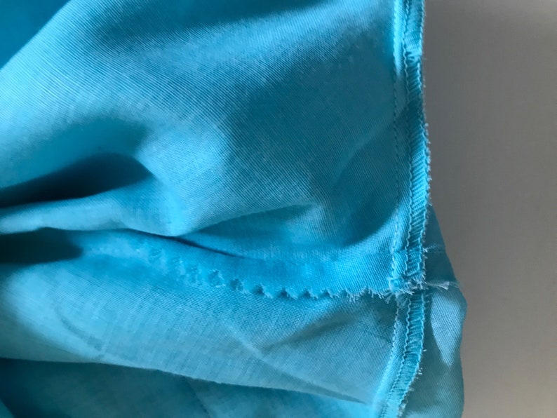 May include: Close-up of a turquoise blue fabric with a stitched seam along the edge.