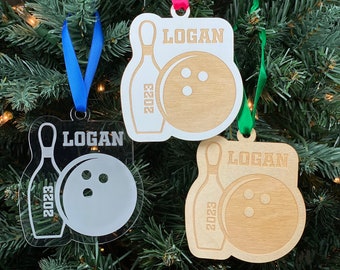 May include: Three personalized Christmas ornaments featuring a bowling pin and bowling ball with the name "Logan" and the year "2023". The ornaments are made of wood and acrylic.