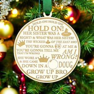 May include: A round wooden Christmas ornament with a gold inscription that reads "Hold on! Hold on! Hold on! Her sister was a right? & What was her sister? The Wicked of the East Bro You're gonna  at me & You're gonna tell me Am I wrong? She wore a & she came down in a Doug Grow up bro Grow up".