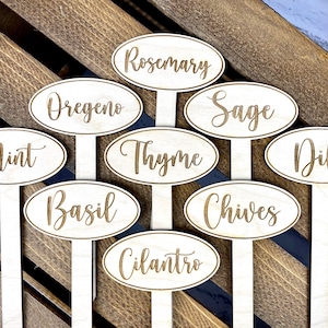 May include: Set of ten wooden plant markers with oval-shaped labels featuring the names of various herbs, including rosemary, oregano, sage, thyme, basil, chives, cilantro, mint, dill, and a blank label.