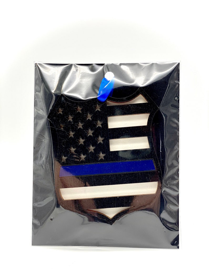 May include: A wooden ornament shaped like a police badge with an American flag design and a blue line across the middle.