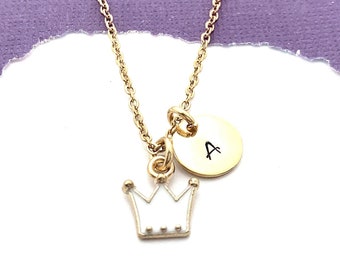 May include: A gold chain necklace with a white crown charm and a gold disc charm with the letter A engraved on it.