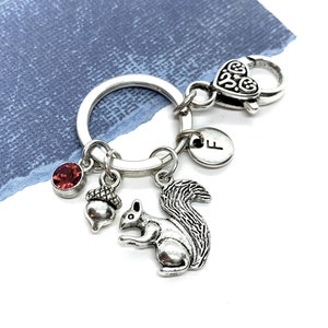 May include: Silver keychain with a squirrel charm, an acorn charm, a red rhinestone, and a silver charm with the letter "F".