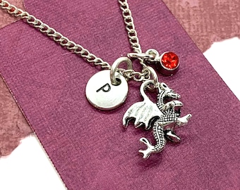 May include: A silver necklace with a dragon charm, a small red gemstone, and a silver disc charm with the letter "P" engraved on it.