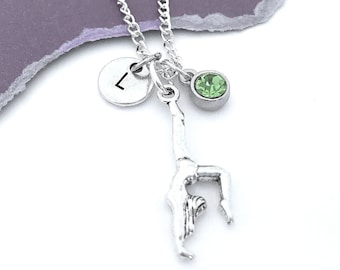 May include: Silver necklace with a gymnast charm, a green crystal charm, and a silver disc charm with the letter L.