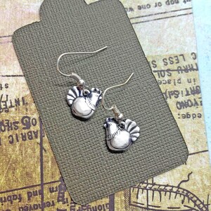 May include: A pair of silver dangle earrings featuring a small chicken design. The earrings are on a brown card.