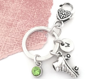 May include: Silver roller skate charm keychain with a green rhinestone, a silver initial charm with the letter "M", and a silver heart charm.