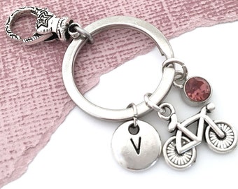 May include: Silver keychain with a bike charm, a letter V charm, and a pink rhinestone. The keychain has a silver lobster clasp.