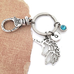 Puede incluir: Llavero de plata con un dije de unicornio, un dije de cristal azul y un dije de plata con la letra "G".