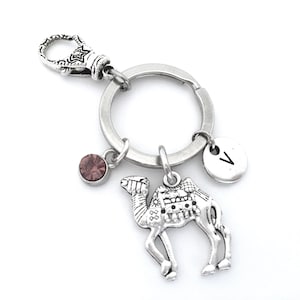 May include: Silver camel keychain with a pink crystal charm and a silver charm with the letter V.