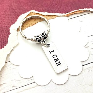 May include: Silver keychain with a decorative ring and a rectangular tag that says "I CAN".