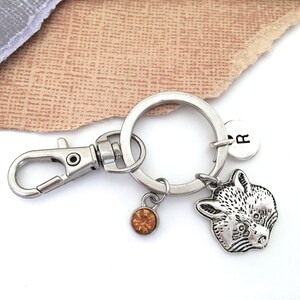 Pu&ograve; includere: Portachiavi in ​​argento con un ciondolo a forma di procione, un piccolo ciondolo di cristallo ambrato e un ciondolo in argento con la lettera "R" su di esso.
