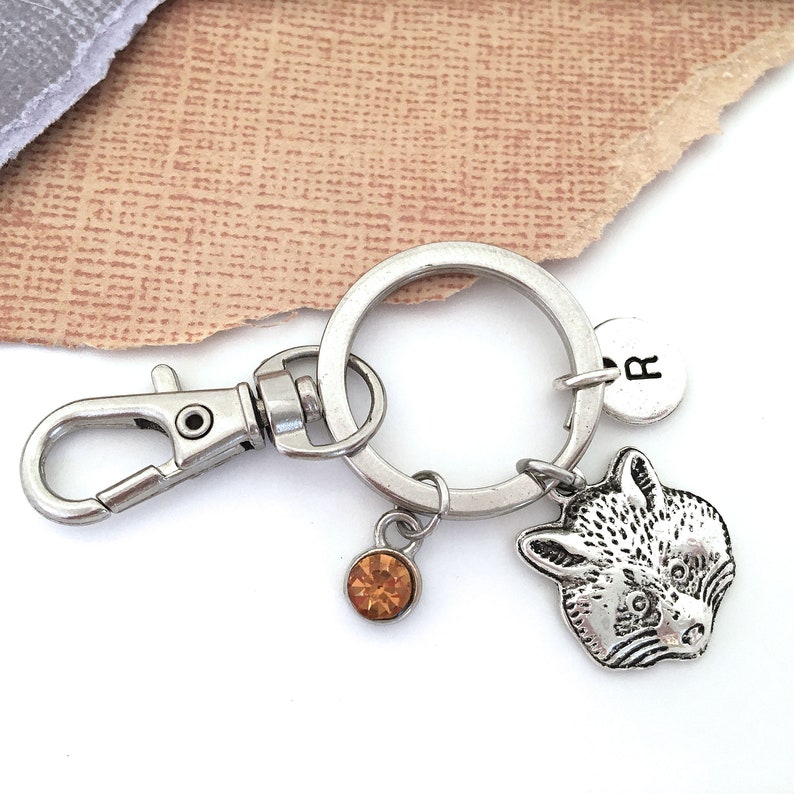 Pu&ograve; includere: Portachiavi in ​​argento con un ciondolo a forma di procione, un piccolo ciondolo di cristallo ambrato e un ciondolo in argento con la lettera "R" su di esso.
