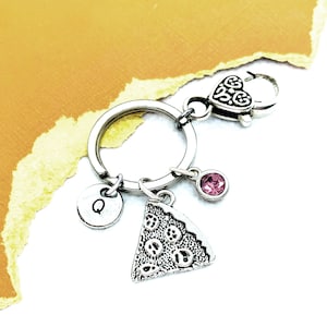 May include: Silver keychain with a pizza charm, a pink rhinestone, and a silver charm with the letter Q.