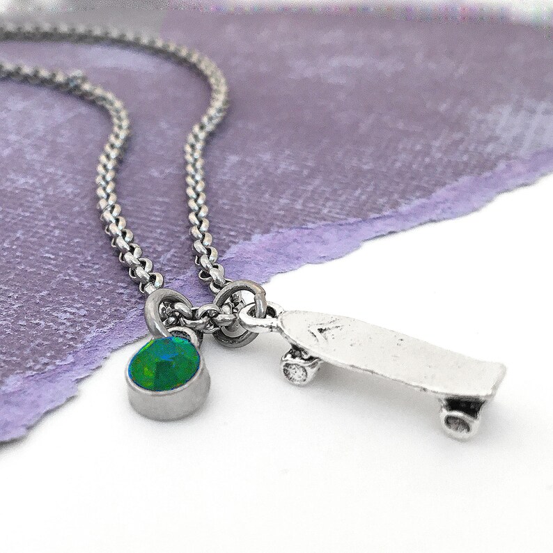 May include: A silver chain necklace with a green gemstone pendant and a silver skateboard charm.