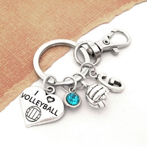 May include: Silver keychain with a heart charm that says "I love volleyball" and a volleyball charm. The keychain also has a blue crystal charm and a silver charm with the letter "G".