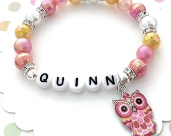 May include: A pink and yellow beaded bracelet with a silver charm that says "QUINN" and a pink owl charm.