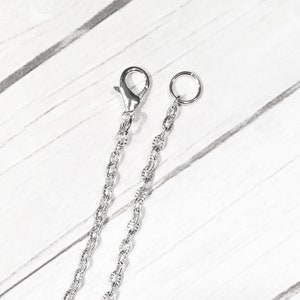 May include: Two silver chains with a lobster clasp and a jump ring. The chains are on a white background.