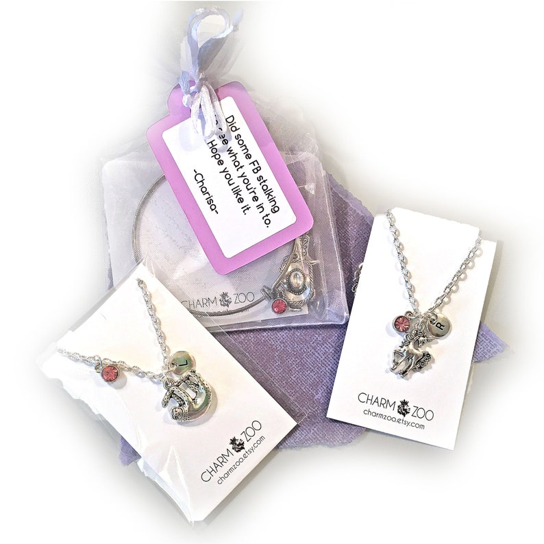 May include: Three silver necklaces with charms on white cards. The charms include a unicorn, a horseshoe, and a letter "J". The necklaces are packaged in a clear plastic bag with a pink tag that says "Did some FB stalking to see what you're in to. Hope you like it. -Charisa- ". The cards have the text "CHARM ZOO charmzoo.etsy.com" printed on them.