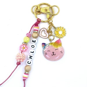 May include: A pink and yellow glitter cat charm keychain with a gold key ring and a beaded name tag that says "CHLOE". The beads are pink, yellow, and white with gold accents.