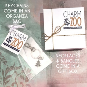 May include: A white gift box with a gold ribbon and the text "CHARM ZOO Personalized Charm Jewelry charmzoo.etsy.com" on the top. A white organza bag with a silver charm keychain featuring a Christmas tree and the text "CHARM ZOO Personalized Charm Jewelry charmzoo.etsy.com" on a tag. The text "KEYCHAINS COME IN AN ORGANZA BAG" is at the top of the image and the text "NECKLACES & BANGLES COME IN A GIFT BOX" is at the bottom of the image.