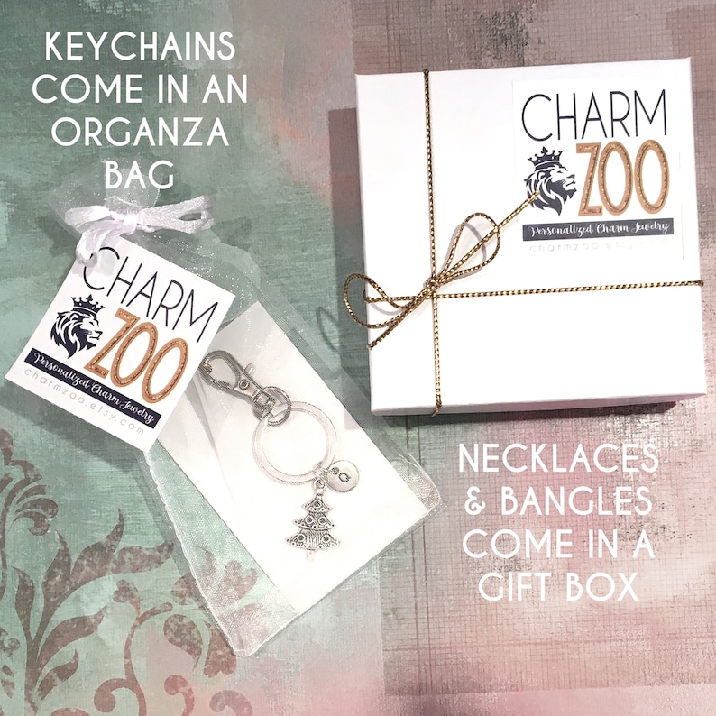 May include: A white gift box with a gold ribbon and the text "CHARM ZOO Personalized Charm Jewelry charmzoo.etsy.com" on the top. A white organza bag with a silver charm keychain featuring a Christmas tree and the text "CHARM ZOO Personalized Charm Jewelry charmzoo.etsy.com" on a tag. The text "KEYCHAINS COME IN AN ORGANZA BAG" is at the top of the image and the text "NECKLACES & BANGLES COME IN A GIFT BOX" is at the bottom of the image.