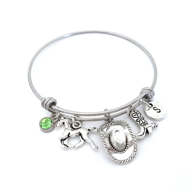 May include: Silver charm bracelet with a green rhinestone, a horse charm, a cowboy hat charm, a boot charm, and a charm with the letter "S".