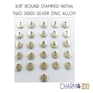 May include: A set of 26 silver-toned metal alphabet charms, each with a letter stamped on the front. The charms are 3/8 inch in diameter and have a small loop at the top for attaching to jewelry or other crafts.