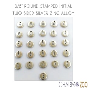 May include: A set of 26 silver-toned metal alphabet charms, each with a letter stamped on the front. The charms are 3/8 inch in diameter and have a small loop at the top for attaching to jewelry or other crafts.