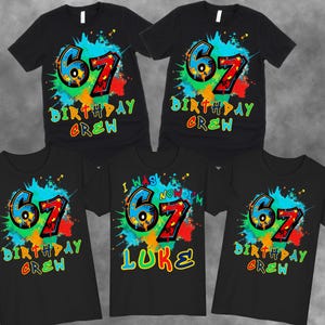 May include: Black t-shirts with a colorful graphic design. The design features the number "67" in blue and red, surrounded by a splash of paint and the words "BIRTHDAY CREW". One shirt says "I WAS NOW I'M 67 LUKE".