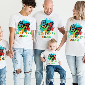 May include: A group of five people wearing matching white t-shirts with a colorful "67 BIRTHDAY CREW" design. The design includes the number 67 in blue and red, with a splash of colors. One shirt says "I HAS NOW 67 LUKE".