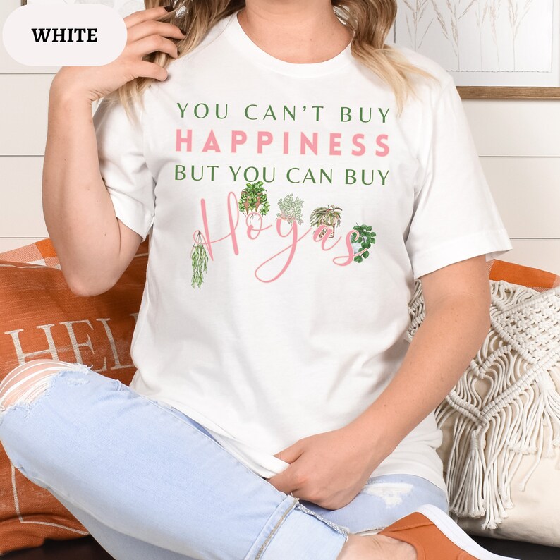 May include: White t-shirt with the text "You can't buy happiness but you can buy Hoyas" in pink lettering. The text is surrounded by illustrations of various plants.