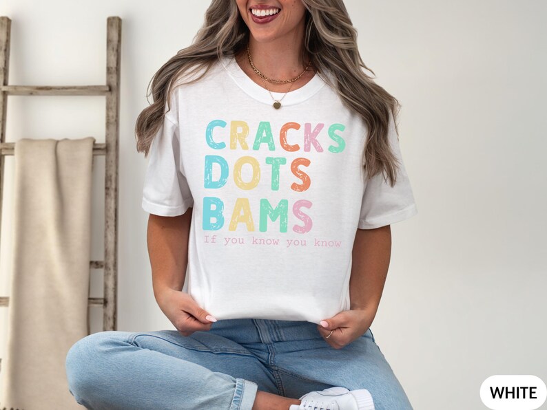 May include: White t-shirt with the words "CRACKS DOTS BAMS" in colorful, pastel letters. Below the words is the phrase "If you know you know". The shirt is a casual, everyday wear item.