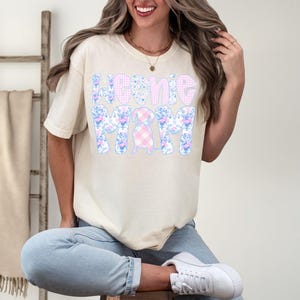 K&ouml;nnte beinhalten: Elfenbeinfarbenes T-Shirt mit dem Text "Home Mom" in einem floralen und Vichy-Muster. Das Design zeigt einen Dackel. Das Shirt hat eine lockere Passform. Dazu werden blaue Jeans und wei&szlig;e Turnschuhe getragen.