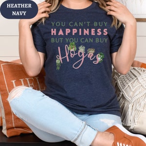 May include: A navy blue t-shirt with the text "You can't buy happiness but you can buy Hogas" in pink lettering. The shirt features a graphic of potted plants.