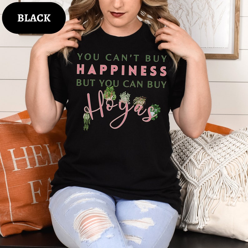 May include: A black t-shirt with the text "You can't buy happiness but you can buy Hoyas" in pink lettering. The shirt features a graphic of several potted hoya plants.