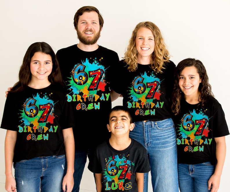 May include: A group of five people wearing matching black t-shirts. Each shirt features a colorful design with the number "67" and the words "Birthday Crew". The design includes splashes of blue, green, red, and yellow.