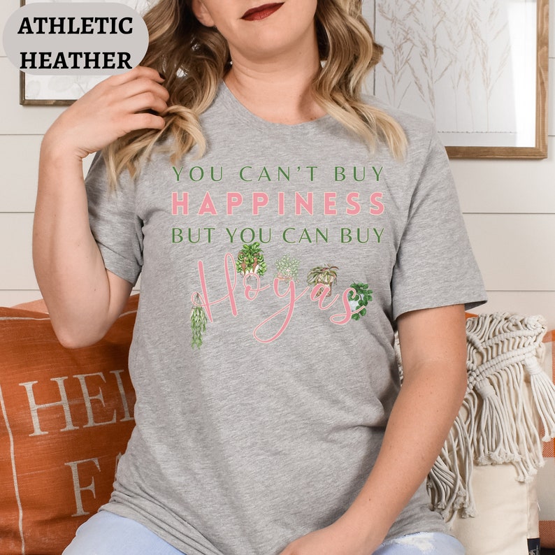 May include: A gray t-shirt with the text "You can't buy happiness but you can buy plants" and the word "Hygge" in pink lettering with illustrations of potted plants.