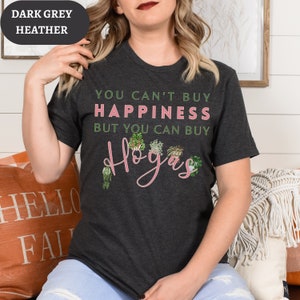 May include: A dark heather grey t-shirt with the text "You can't buy happiness but you can buy plants" and a pink graphic of the word "plants" with illustrations of potted plants.