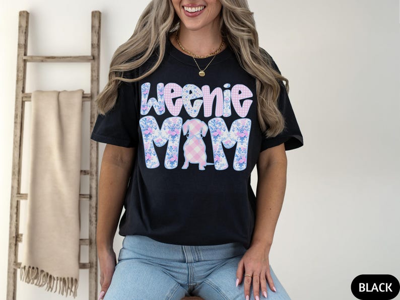 K&ouml;nnte beinhalten: Schwarzes T-Shirt mit dem Text "Weenie Mom" in einem floralen und karierten Design. Das Shirt zeigt eine Dackel-Hunde-Illustration. Das Wort "BLACK" befindet sich in einem schwarzen Rechteck unten rechts.